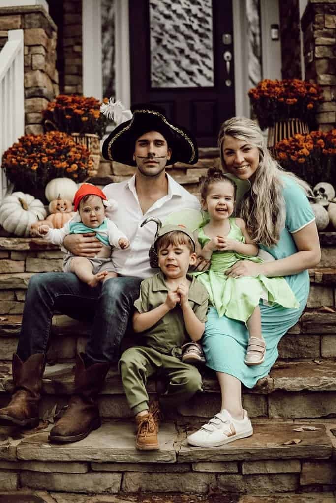 A family of five dressed in Peter Pan themed costumes for Halloween. The family includes Peter Pan, Wendy, Captain Hook, Tinker Bell, and Mr. Smee.