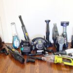 An assortment of handheld vacuums designed for pet hair removal are displayed on a wooden floor next to a black cat, showcasing various models and attachments.