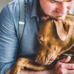 man comforting his sad dog with a hug.