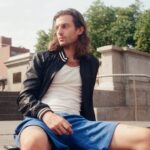 Peter Vack photographed in a casual pose, highlighting his braided hair and informal attire, reflecting a relaxed and creative persona.