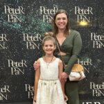 A mother and daughter pose at a Peter Pan Broadway photo booth at the Straz Center theater in Tampa, Florida, celebrating their family theater experience.