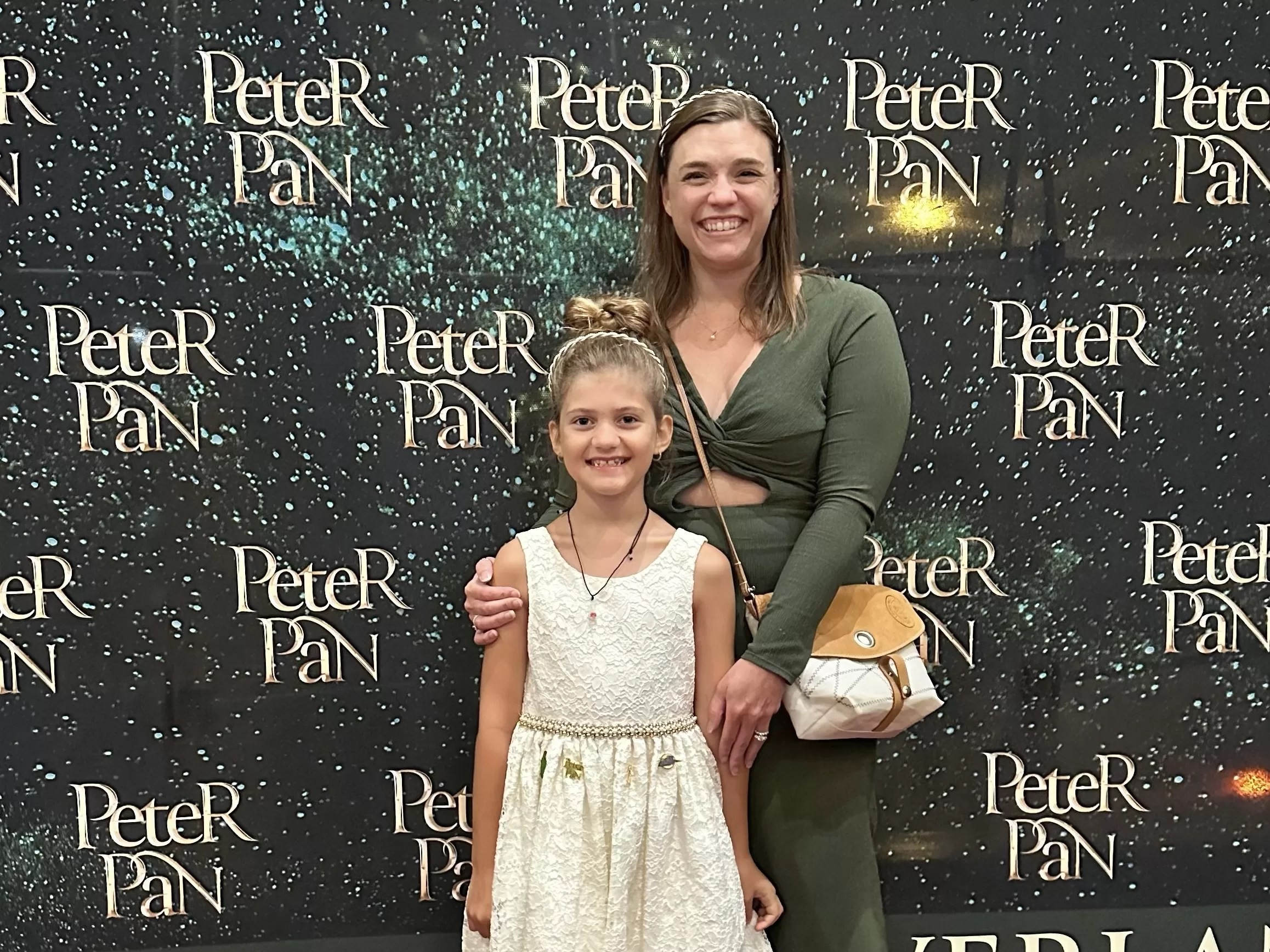 A mother and daughter pose at a Peter Pan Broadway photo booth at the Straz Center theater in Tampa, Florida, celebrating their family theater experience.