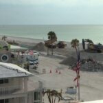 Coastal view of St. Pete Beach, Florida, showcasing the aftermath of a hurricane near Hurricane Restaurant, with sand dunes reaching building height illustrating the storm's impact and ongoing recovery efforts.