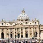 An expansive view of St Peter's Piazza in Vatican City, showcasing the colonnade and obelisk under a bright sky.