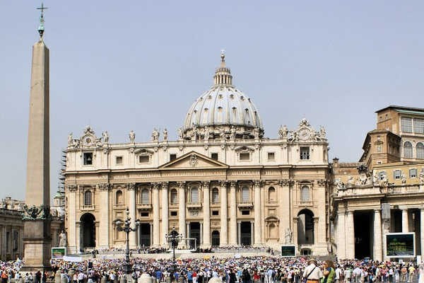 An expansive view of St Peter's Piazza in Vatican City, showcasing the colonnade and obelisk under a bright sky.