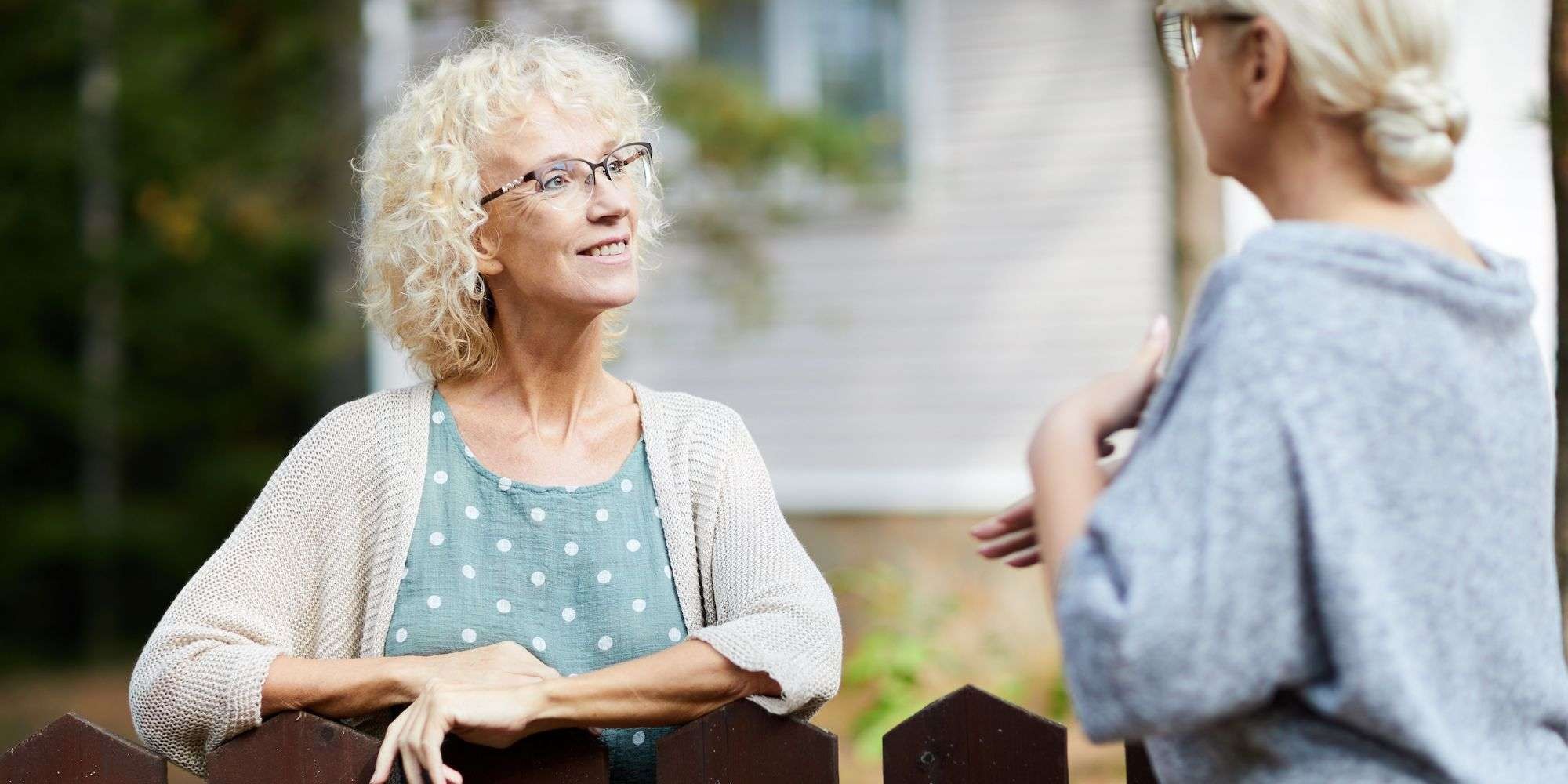 Neighbors chat amicably over a fence, emphasizing the importance of communication and community in managing backyard chickens.