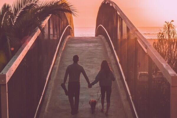 A couple walking their dog on a beach boardwalk, representing a peaceful setting for euthanasia